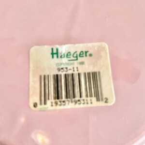 May include: A pink ceramic plate with a white rim and a white sticker with the text "Haeger" and a barcode. The barcode number is 19557195311.