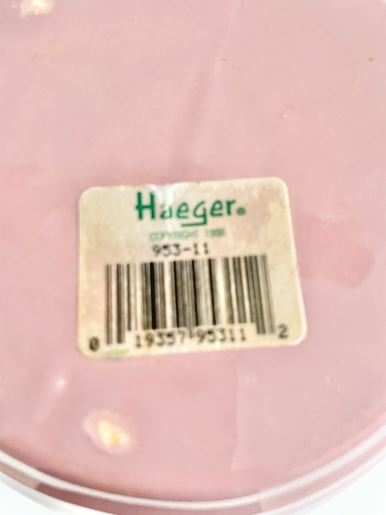 May include: A pink ceramic plate with a white rim and a white sticker with the text "Haeger" and a barcode. The barcode number is 19557195311.