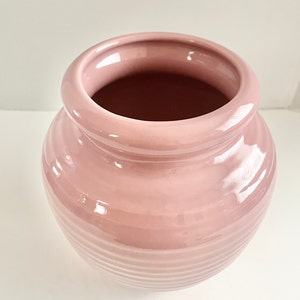 May include: A pink ceramic vase with a ribbed design. The vase has a wide mouth and a rounded body.