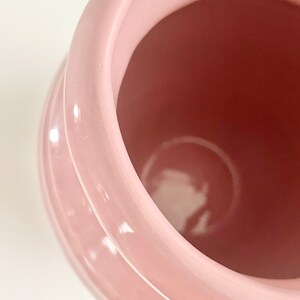 May include: A pink ceramic vase with a smooth, glossy finish. The vase has a wide opening and a rounded shape.