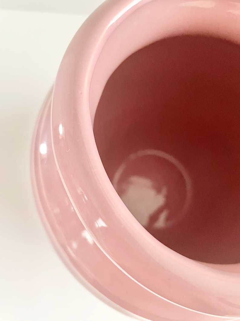 May include: A pink ceramic vase with a smooth, glossy finish. The vase has a wide opening and a rounded shape.