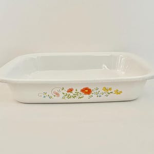 Puede incluir: Fuente rectangular blanca para hornear con esquinas redondeadas. La fuente presenta un diseño floral con flores rojas, amarillas y azules. La fuente está hecha de un material brillante y tiene un borde ligeramente elevado.