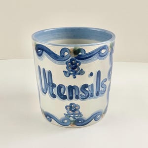 May include: A white ceramic mug with a black handle and the text "But First, Coffee" in a black, handwritten-style font. The mug is on a white surface.