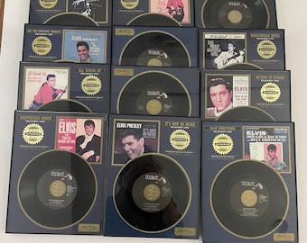May include: A collection of framed Elvis Presley records. Each frame features a black vinyl record, a vintage photo of Elvis, and text indicating the song title and release year. The frames are navy blue with gold accents.