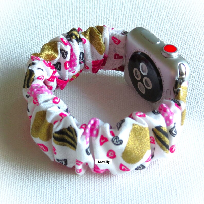 May include: A white, pink, and gold patterned fabric watch band with a silver Apple Watch.
