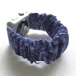 May include: A silver smartwatch with a blue and purple patterned fabric band. The band is gathered, creating a textured appearance. The watch face is visible, showing the screen and side button.