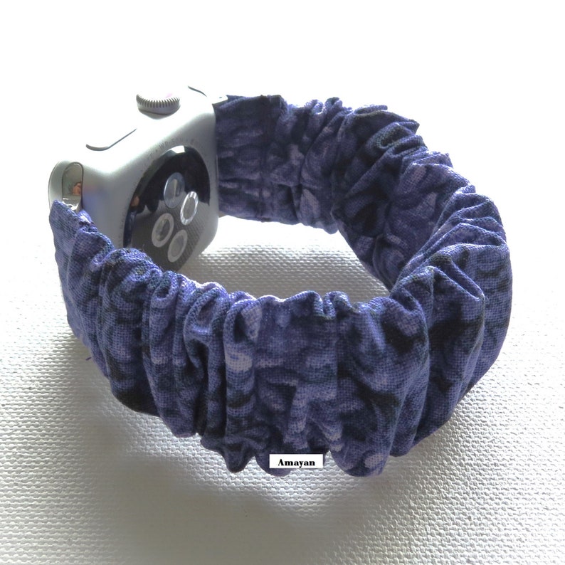 May include: A silver smartwatch with a blue and purple patterned fabric band. The band is gathered, creating a textured appearance. The watch face is visible, showing the screen and side button.