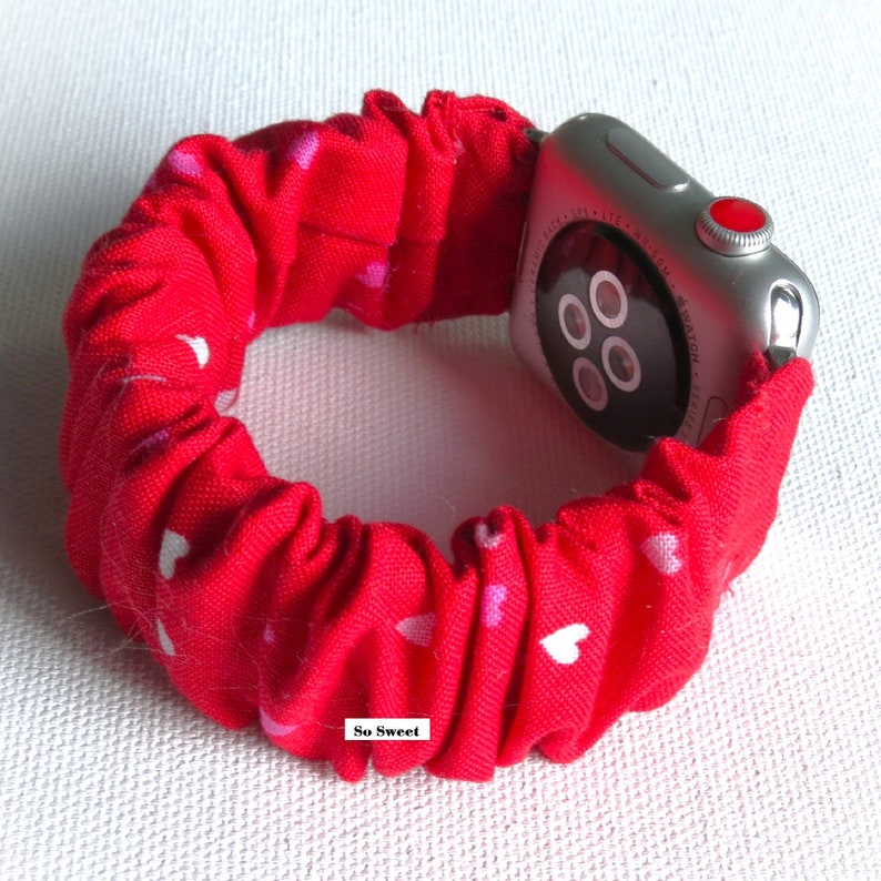 May include: Red Apple Watch band with a white heart pattern. The band is made of a stretchy fabric and has a 'So Sweet' label.