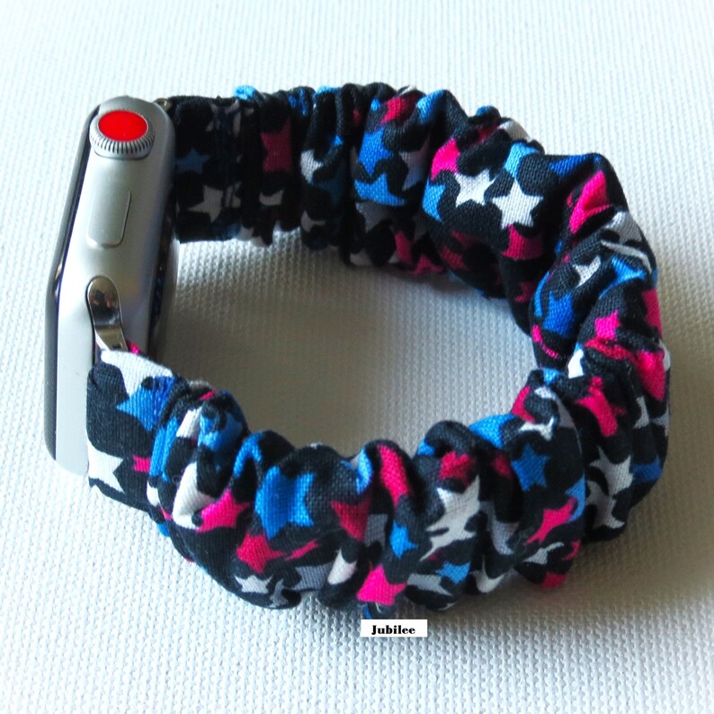 Op de afbeelding: Een zwart, blauw en roze Apple Watch-bandje met witte sterren. Het bandje is gemaakt van rekbaar materiaal en is ontworpen om strak om de pols te passen.