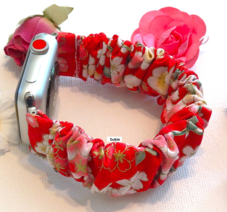 K&ouml;nnte beinhalten: Rotes und wei&szlig;es Blumenmuster-Armband f&uuml;r Apple Watch mit silbernem Apple Watch-Zifferblatt. Das Armband ist aus Stoff und hat ein dehnbares, elastisches Gef&uuml;hl. Das Armband wird auf wei&szlig;em Hintergrund gezeigt.