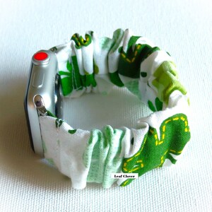 Peut inclure: Un bracelet de montre Apple blanc et vert &agrave; motif tr&egrave;fle. Le bracelet est en tissu et a une forme extensible et r&eacute;glable. Le bracelet est pr&eacute;sent&eacute; sur une Apple Watch argent&eacute;e.