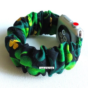 Peut inclure: Un bracelet de montre noir et vert avec un motif trèfle. Le bracelet est en tissu et a un design de type scrunchie. Le texte "Luck of the Irish" est visible sur le bracelet.