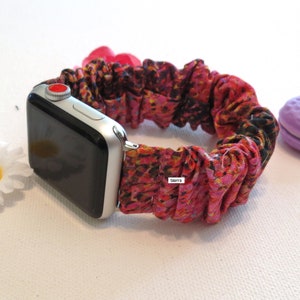 May include: A scrunchie Apple Watch band with a vibrant floral pattern in shades of red, pink, yellow, and black. The band is attached to a silver Apple Watch. The word "Sierra" is visible on the band.