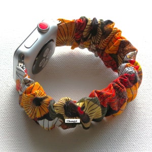 K&ouml;nnte beinhalten: Ein farbenfrohes Apple Watch Armband aus Stoff mit einem floralen Muster in Orange-, Gelb-, Gr&uuml;n- und Schwarzt&ouml;nen. Das Armband ist aus dehnbarem Material und tr&auml;gt ein "Changyi"-Etikett.