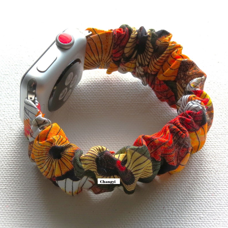 K&ouml;nnte beinhalten: Ein farbenfrohes Apple Watch Armband aus Stoff mit einem floralen Muster in Orange-, Gelb-, Gr&uuml;n- und Schwarzt&ouml;nen. Das Armband ist aus dehnbarem Material und tr&auml;gt ein "Changyi"-Etikett.