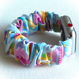 May include: A colorful, patterned fabric Apple Watch band with a blue, pink, yellow, and green design. The band is made of a stretchy, elastic material and has a "Spring Chic" label.