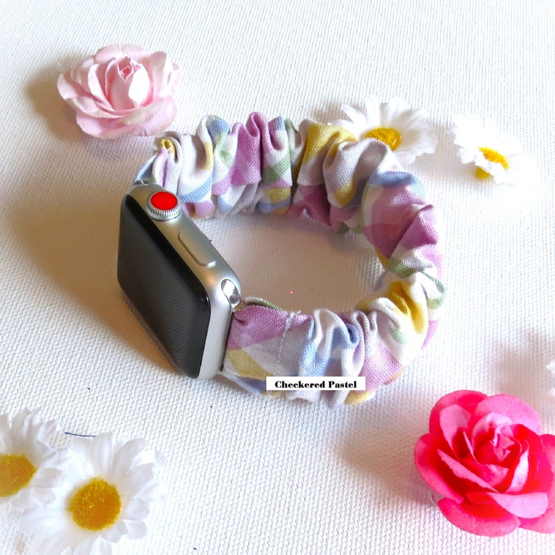 May include: A colorful checkered pastel fabric Apple Watch band. The band is made of a soft, stretchy fabric and is designed to fit most wrist sizes. The band is shown on a silver Apple Watch.