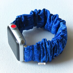 Op de afbeelding: Een blauwe stoffen Apple Watch band met een zilveren Apple Watch. De band is gemaakt van een rekbaar, elastisch materiaal en heeft een gerimpelde uitstraling.
