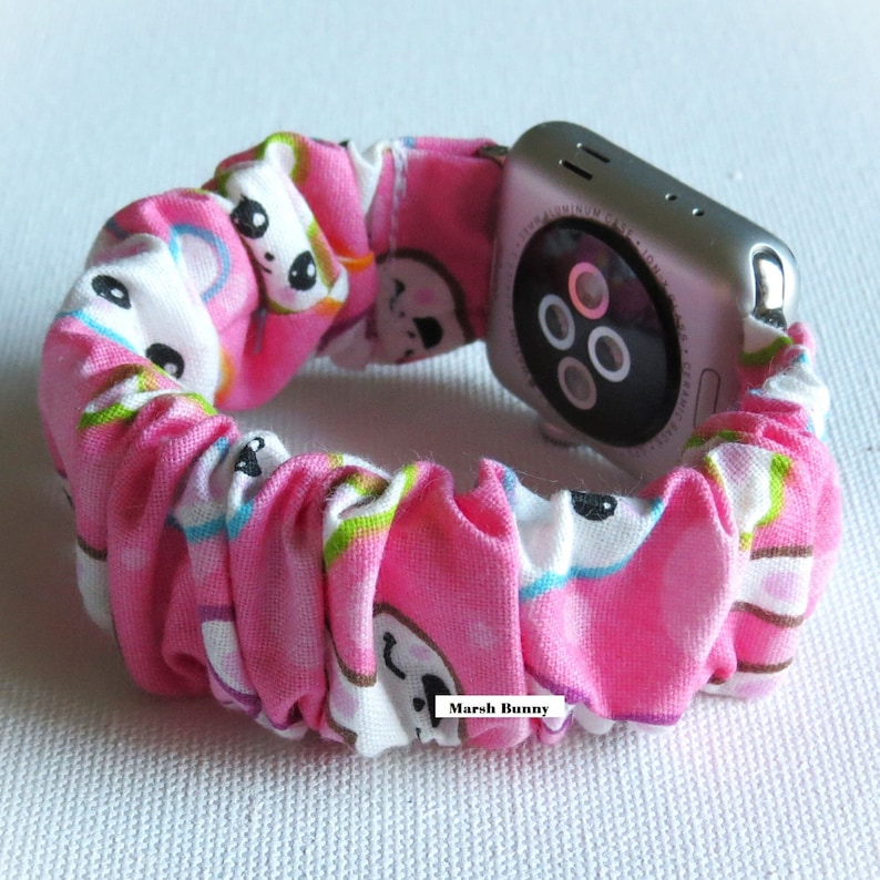 May include: Pink and white Apple Watch band with a cartoon bunny pattern. The band is made of fabric and has a stretchy, adjustable fit. The text "Marsh Bunny" is printed on the band.