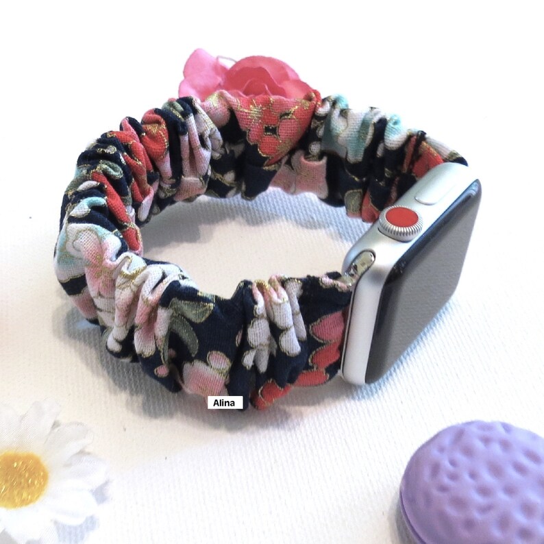 K&ouml;nnte beinhalten: Ein schwarzes und wei&szlig;es Blumenmuster-Armband f&uuml;r die Apple Watch mit einem roten Knopf auf dem Zifferblatt der Uhr. Das Armband ist aus Stoff und hat einen ger&uuml;schten Look. Der Text "Alina" ist auf dem Armband sichtbar.