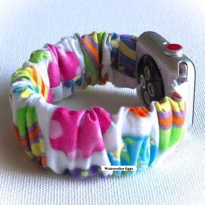 May include: A colorful fabric watch band with a white background and a pattern of watercolor eggs. The band is attached to a silver Apple Watch.