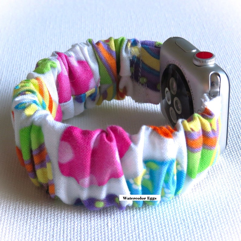 May include: A colorful fabric watch band with a white background and a pattern of watercolor eggs. The band is attached to a silver Apple Watch.