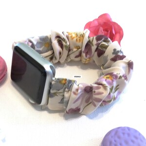 May include: A floral patterned Apple Watch band with a pink flower accent. The band is made of a soft, stretchy fabric and is designed to fit most Apple Watch sizes.