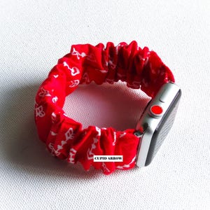 May include: Red and white patterned fabric Apple Watch band with the text "CUPID ARROW" printed on the band.