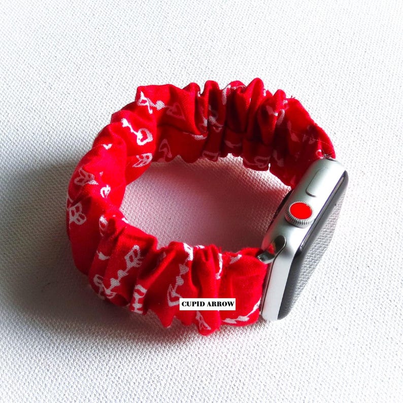 May include: Red and white patterned fabric Apple Watch band with the text "CUPID ARROW" printed on the band.