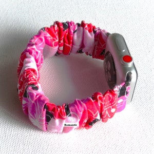 May include: A pink, red, and black floral patterned fabric Apple Watch band. The band is made of a stretchy material and is designed to fit snugly around the wrist. The band is shown on a silver Apple Watch.
