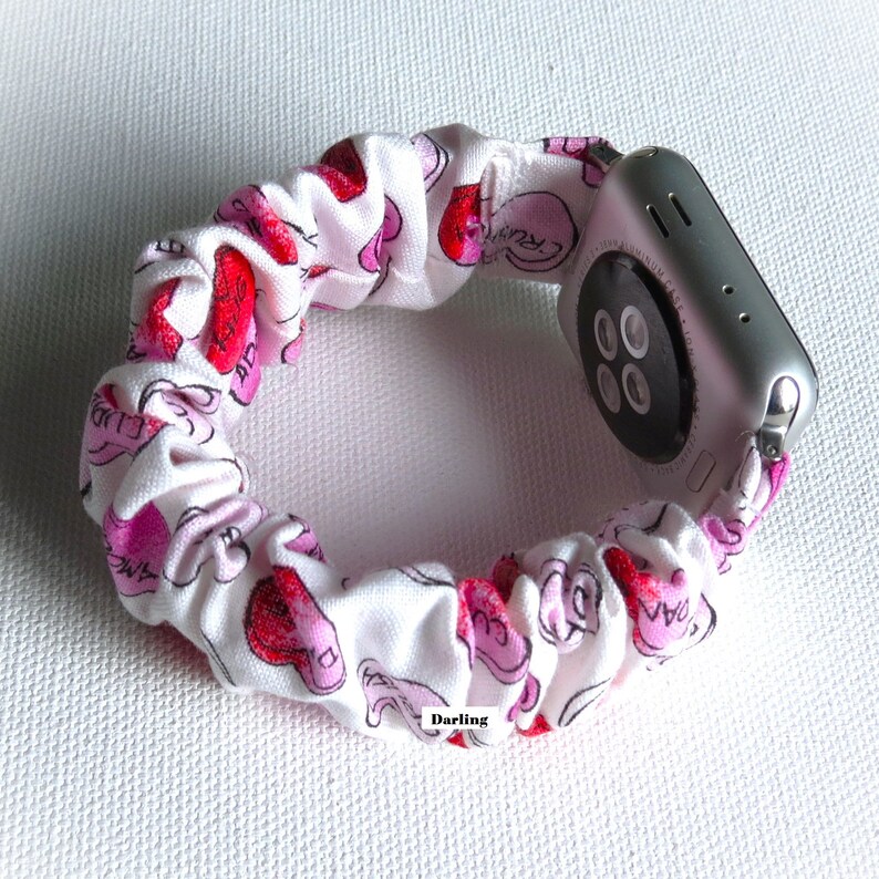 May include: White and pink fabric watch band with a pink and white heart pattern. The band is made of a stretchy material and is designed to fit around a smartwatch.