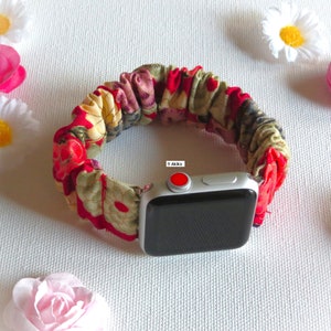 K&ouml;nnte beinhalten: Ein Armband aus rotem, gr&uuml;nem und gelbem Stoff mit Blumenmuster f&uuml;r eine Apple Watch. Das Armband besteht aus einem weichen, dehnbaren Material und hat einen roten Knopf an der Seite.