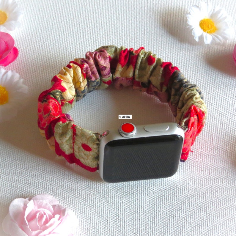 K&ouml;nnte beinhalten: Ein Armband aus rotem, gr&uuml;nem und gelbem Stoff mit Blumenmuster f&uuml;r eine Apple Watch. Das Armband besteht aus einem weichen, dehnbaren Material und hat einen roten Knopf an der Seite.