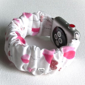 May include: White Apple Watch band with a pink and gray heart pattern. The band is made of a soft, stretchy fabric and has a ruffled design. The text "Lovely" is printed on the band.