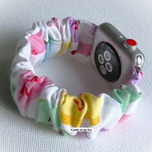 May include: A colorful fabric watch band with a white background and stripes of pink, yellow, green, and purple. The band is wrapped around a silver Apple Watch.