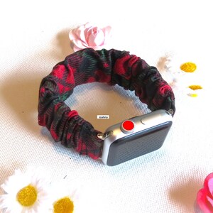 May include: A red and green plaid fabric watch band for an Apple Watch. The band is made of a stretchy, elastic material and has a red button on the watch face.