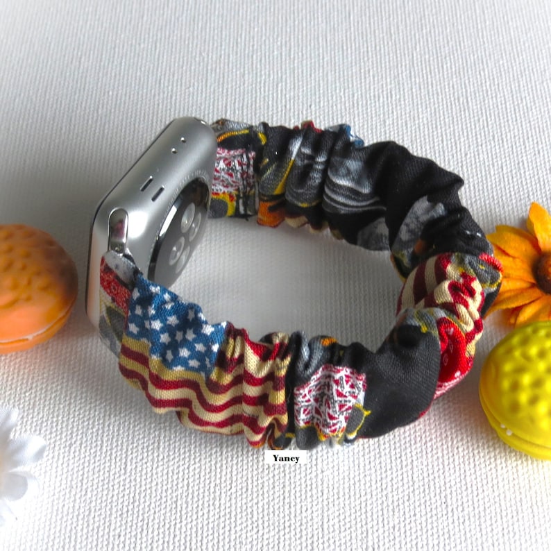 Op de afbeelding: Een kleurrijk Apple Watch bandje van stof met een Amerikaans vlagontwerp en een zwarte achtergrond. Het bandje is gemaakt van rekbaar materiaal en is ontworpen om te passen op verschillende polsmaten.