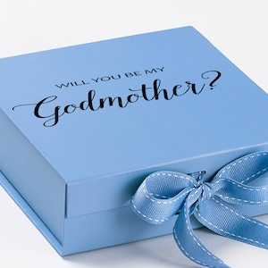 May include: A light blue gift box with a white satin ribbon tied in a bow. The box has the text "Will you be my Godmother?" printed on the top.