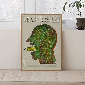Puede incluir: Un sofá marrón claro con un cojín blanco y un póster enmarcado con el texto "TEACHER'S PET" y una ilustración verde y amarilla de una persona con un lápiz en la boca.