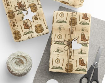 May include: Gift-wrapped presents with camping-themed paper. The paper features illustrations of tents, backpacks, boots, and compasses. Each package is tied with twine and a white tag. A ball of twine, scissors, and blank tags are also visible.