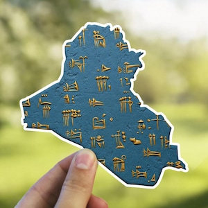 May include: A blue vinyl sticker shaped like the outline of Iraq with gold cuneiform script on the surface.