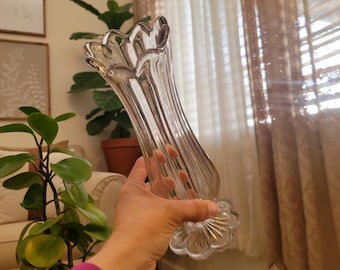 May include: A clear glass vase with a fluted design. The vase has a wide mouth and a rounded base.