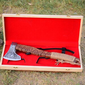 May include: A hand-crafted axe with a wooden handle and a detailed metal head, displayed in a wooden box with a red velvet lining.