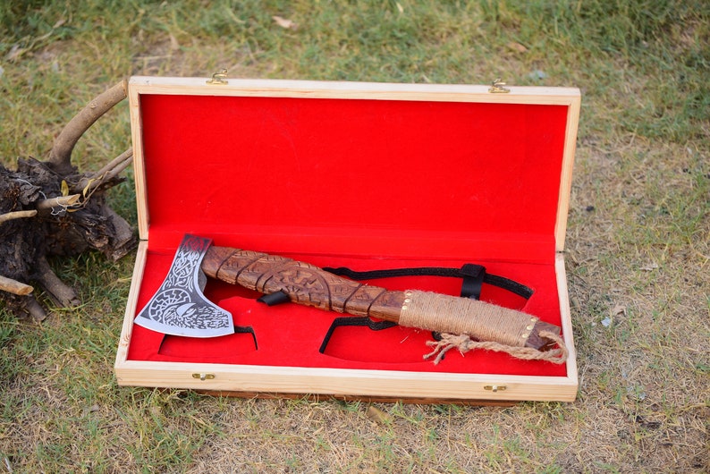 May include: A hand-crafted axe with a wooden handle and a detailed metal head, displayed in a wooden box with a red velvet lining.