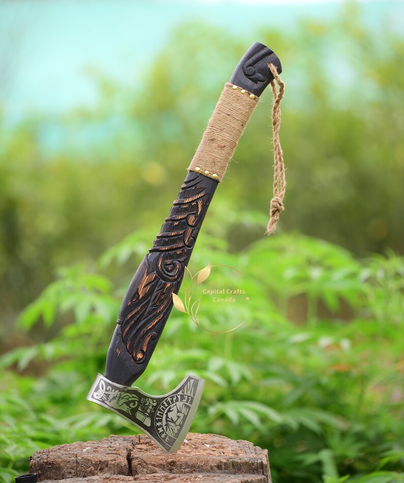 May include: A black wooden axe with a carved handle and a silver blade. The blade has a skull and runes engraved on it. The axe is on a wooden stump with a green background.