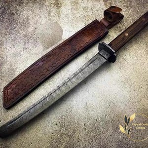 May include: A Japanese-style tanto knife with a patterned steel blade and a dark wooden handle. The knife is accompanied by a brown leather sheath with embossed detailing. The blade is approximately 25 cm long.
