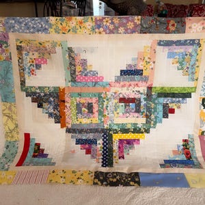 May include: A quilt with a heart-shaped pattern made from colorful fabric squares. The quilt is made in a log cabin style with a white background.