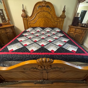 Puede incluir: Una colcha con un patrón geométrico de cuadrados negros, grises y blancos con detalles en rojo, colocada sobre una gran estructura de cama de madera con cabecero y piecero arqueados. La colcha tiene un borde negro y un diseño de diamantes.