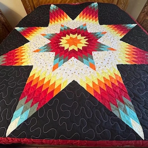 May include: A quilt featuring a large central Lone Star pattern composed of diamond-shaped fabric pieces in shades of yellow, orange, red, and teal. The star is set against a black background with a continuous meandering stitch pattern throughout.