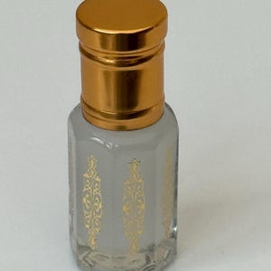 Pode incluir: Frasco de perfume pequeno, de vidro transparente, com tampa dourada. O frasco tem padr&otilde;es decorativos dourados na frente. Projetado para conter perfume ou &oacute;leos essenciais.
